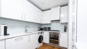 Une cuisine moderne avec des meubles blancs, un lave-linge, un four et une machine à café.