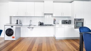 A modern kitchen with white cabinets, a washing machine, a sink, a stove, and a microwave. - PBC | One Bedroom Apartment with Balcony JT6 (London)