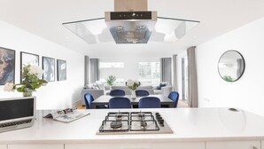 Ett modernt kök med en köksö i mitten, en matplats med blå stolar och ett stort fönster.