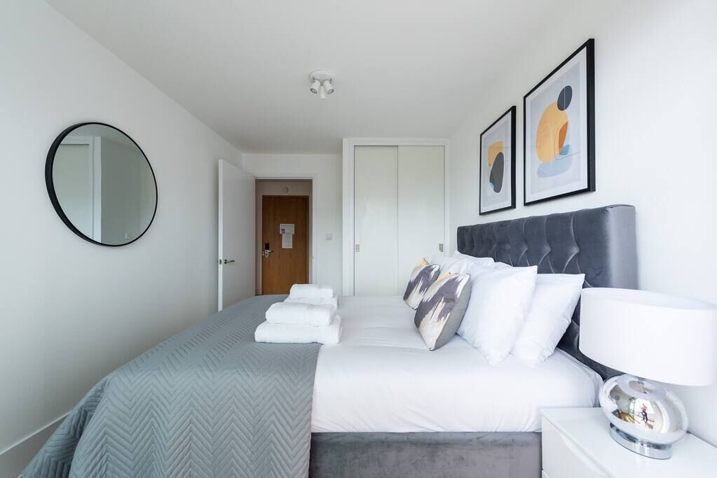 Ein modernes Schlafzimmer mit einem großen Bett, einem runden Spiegel und zwei gerahmten Kunstwerken an der Wand.