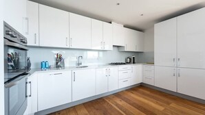A modern kitchen with white cabinets, a stainless steel oven, and a wooden floor. - PBC | Three Bedroom Apartment with Balcony JT9 (London)