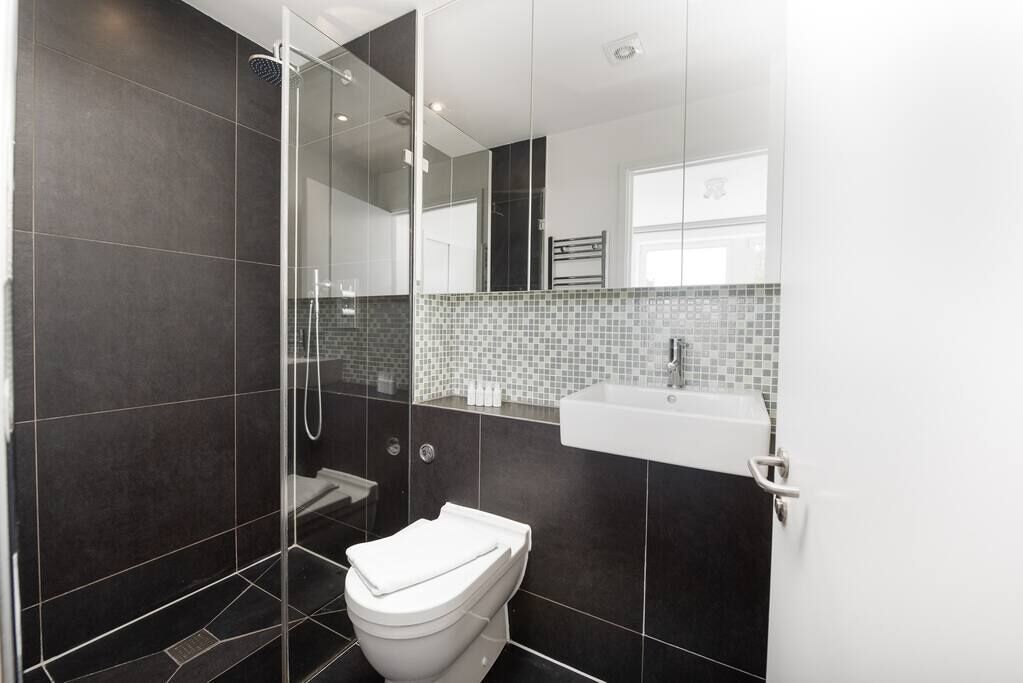 A modern bathroom with a glass shower enclosure, a white toilet, and a tiled backsplash.
