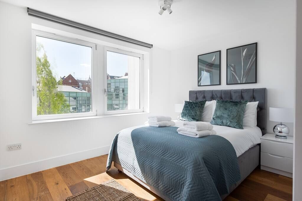 Un dormitorio con una cama, una mesita de noche, una ventana y dos cuadros colgados en la pared.