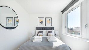 A modern bedroom with a large bed, two bedside tables, a round mirror, and framed artwork on the wall. - PBC | Three Bedroom Apartment with Balcony JT9 (London)