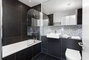 Une salle de bain moderne avec une douche à parois de verre, une baignoire blanche, un lavabo avec un pare-éclaboussures carrelé et des toilettes.