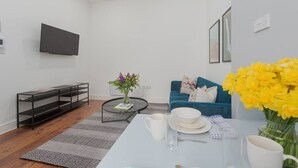A modern living room with a sofa, a coffee table, and a TV mounted on the wall. - PBC | One Bed Apartment Earl's Court 121 EC2 (London)