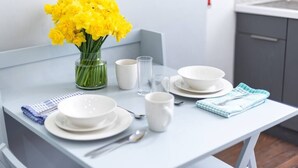 A dining table with white plates, bowls, and a vase of yellow flowers. - PBC | One Bed Apartment Earl's Court 121 EC2 (London)