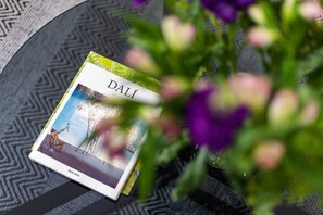 A book titled 'DALÍ' sits on a round table with a geometric patterned tablecloth, accompanied by a vase with fresh flowers.