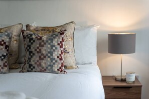 Restful retreat with a bed dressed in crisp white linens, flanked by two unique pillows and a modern nightstand.