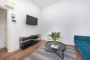 Relax in this stylish living room with a flat-screen TV, book, and vase of flowers on a round coffee table.