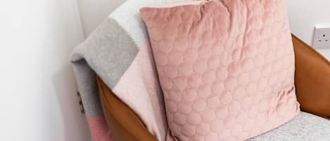 A chair with a grey and pink quilted pillow and a grey blanket.