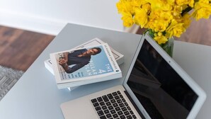 Un ordinateur portable est posé sur une table, à côté d’un livre intitulé « Le plan des quatre piliers » et d’un vase rempli de fleurs jaunes.