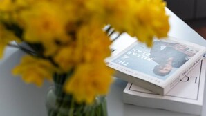 Un livre intitulé « THE PILLAR PLAN » est posé sur une table, avec un vase de fleurs jaunes en premier plan.