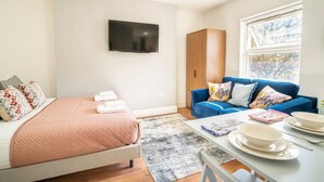 Ett modernt sovrum med en säng, en blå soffa, en tv och ett fönster med utsikt.