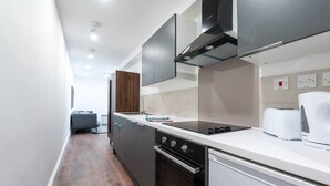 A modern kitchen with dark cabinetry, a white countertop, and a built-in oven. - PBC | Studio Apartment Earl's Court 119C ECA1 (London)