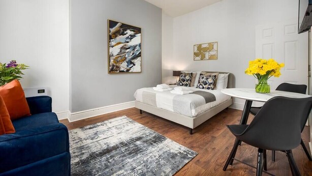 Une chambre à coucher moderne avec un lit, un canapé bleu, une table à manger et un vase rempli de fleurs jaunes.