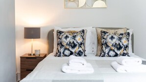 Un lit bien fait, agrémenté de deux coussins à motifs, d’une lampe de chevet et d’une œuvre d’art accrochée au mur au-dessus.