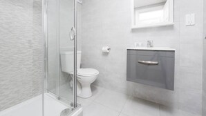 Une salle de bain moderne dotée d’une douche à parois de verre, de toilettes et d’un meuble-lavabo avec un miroir.