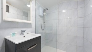 A modern bathroom with a white sink, dark cabinet, and a glass shower enclosure. - PBC | One Bed Earl's Court ECC3 (London)