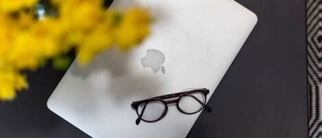 A laptop with a pair of glasses on top, placed on a dark surface with yellow flowers in the background.