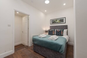 Un dormitorio con cama, puerta y un cuadro en la pared.