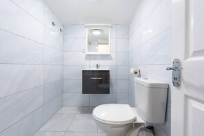A small, modern bathroom with white tiles, a white toilet, a black cabinet, and a mirror above the sink.