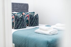 A neatly made bed with a blue blanket and multiple pillows, including patterned and solid colors.
