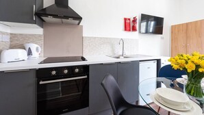 A modern kitchen with a stove, oven, and built-in microwave. There is a sink with a faucet, a black range hood, and a flat-screen TV mounted above the sink.