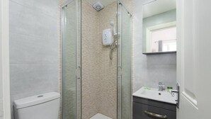 A modern bathroom with a glass-enclosed shower, a white toilet, a sink with a mirror, and a dark cabinet.