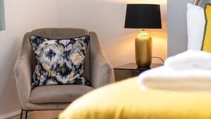 Een slaapkamer met een bed, een stoel, een lamp en een kussen.