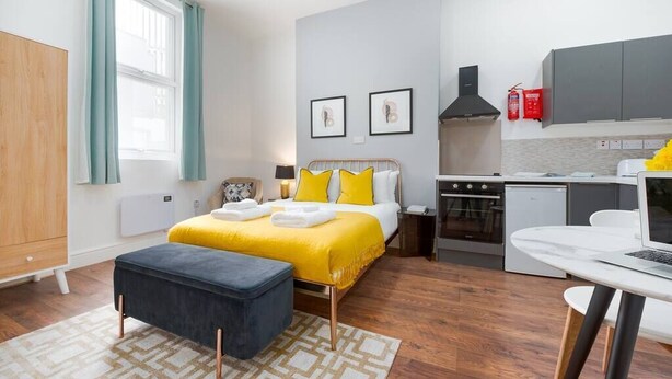 Een moderne slaapkamer met een bed, nachtkastje en een kleine keukenhoek.