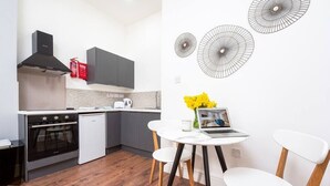 Een moderne keuken met grijze kastjes, een zwarte afzuigkap en een vaatwasser. Er staat een witte tafel met twee stoelen en een laptop.