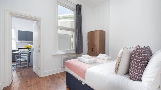 A bedroom with a bed, a wooden wardrobe, a desk with a chair, and a window with curtains. - PBC | Cosy 1-Bed Apt - Earl's Court 119 - EC3 (London)