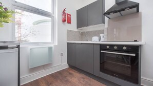Een moderne keuken met grijze kastjes, een ingebouwde oven en een raam met uitzicht op een bouwplaats.