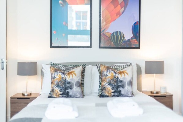 Une chambre d’hôtel comprenant un lit, deux tables de chevet, deux lampes et deux oreillers aux motifs tropicaux.