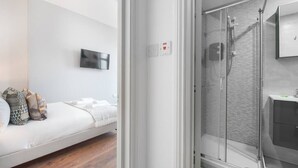 A modern room with a bed, a mounted TV, and a glass-enclosed shower area. - PBC | Large Studio - Earl's Court 119 - EC6 (London)