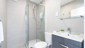 A modern bathroom with a glass-enclosed shower, a white toilet, and a vanity with a mirror and sink. - PBC | Studio Apartment Earl's Court 119 EC7 (London)
