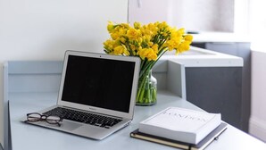 A laptop on a desk with a vase of yellow flowers and a book titled "LONDON". - PBC | Studio Apartment Earl's Court 119 EC7 (London)