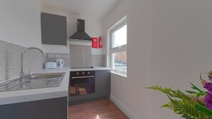 A compact kitchen with a sink, stove, and window. - PBC | Studio Apartment Earl's Court 119 EC7 (London)