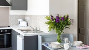 Een compacte keuken met een inbouwvaatwasser, een spoelbak en een klein eethoekje met een tafel voor twee personen.