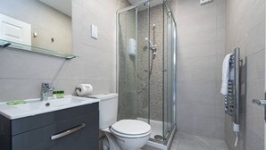 Een moderne badkamer met een douchecabine van glas, een wit toilet en een wastafelmeubel met een wastafel en opbergruimte.