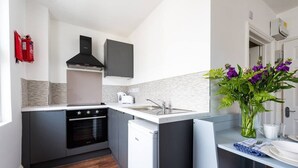 Een moderne keuken met grijze kasten, een zwarte afzuigkap, een witte koelkast en een klein eiland met een spoelbak.
