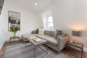 Relax in this stylish living room with a comfortable sofa, side table, and coffee table, surrounded by a large mirror and a potted plant.