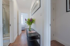 Enter a serene hallway with a console table and framed artwork, leading to a bathroom with a shower.