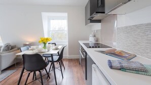 A modern kitchen with a dining area, white cabinetry, and a window providing natural light. - PBC | Two-Bed Apt - Earl's Court 119 - EC9 (London)
