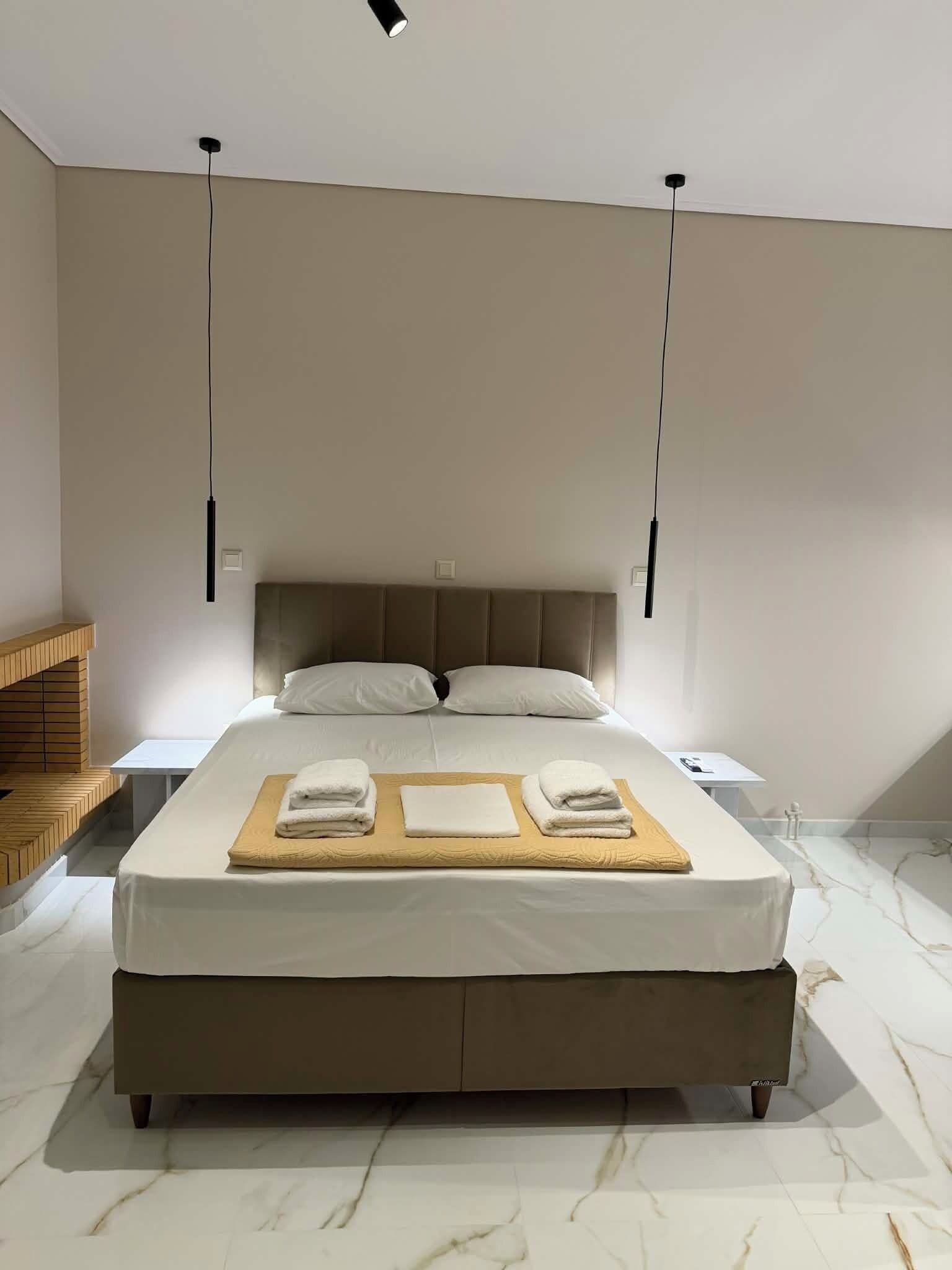 A modern bedroom with a large bed, two bedside tables, a wooden bench, and a marble floor.