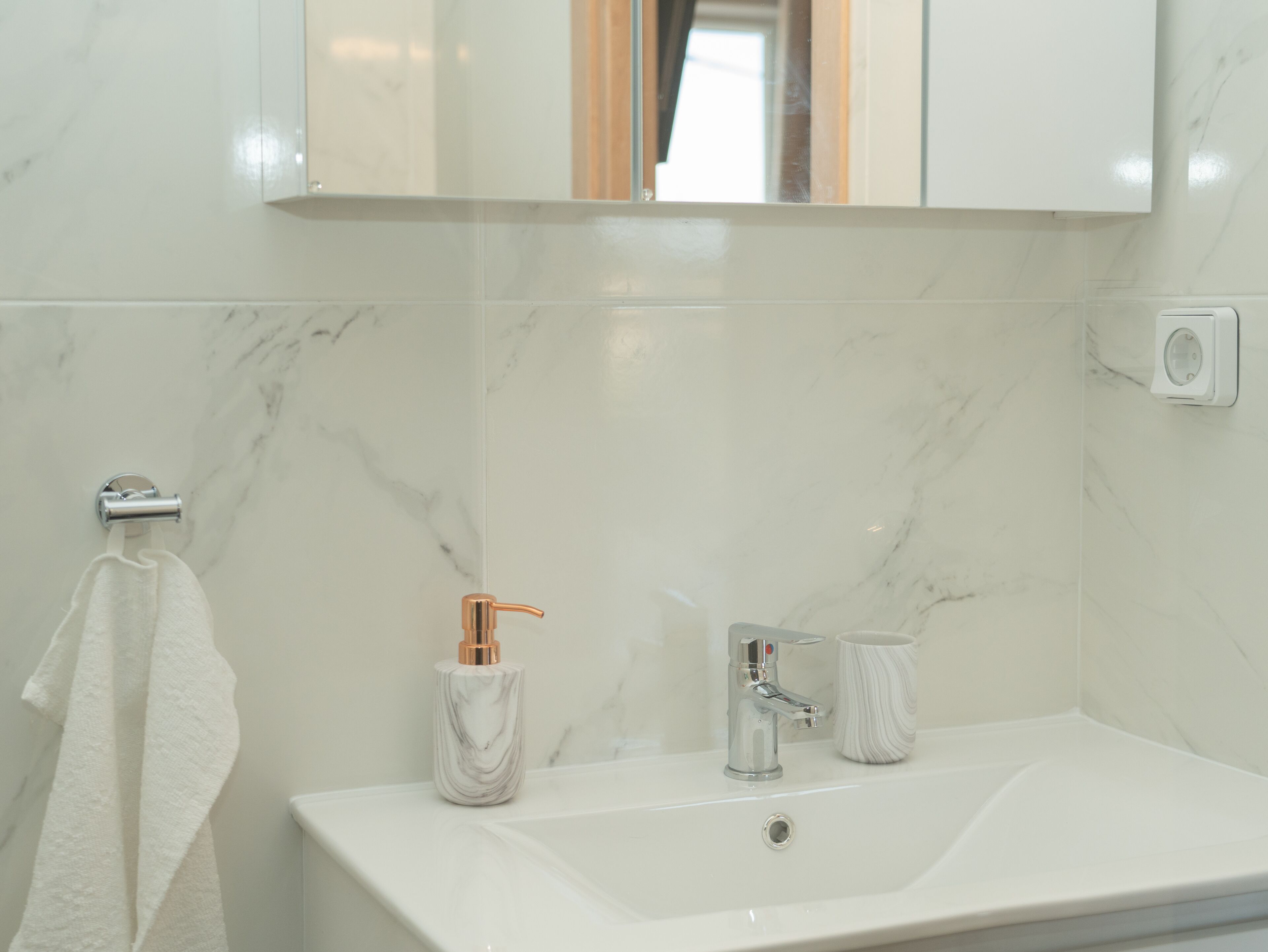A bathroom with a white marble sink, a mirror above it, a towel hanging on a rack, and a soap dispenser.