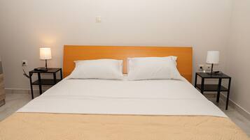 A neatly made bed with a beige bedspread, two white pillows, and an orange headboard. There are two bedside tables, each with a lamp and a power outlet.