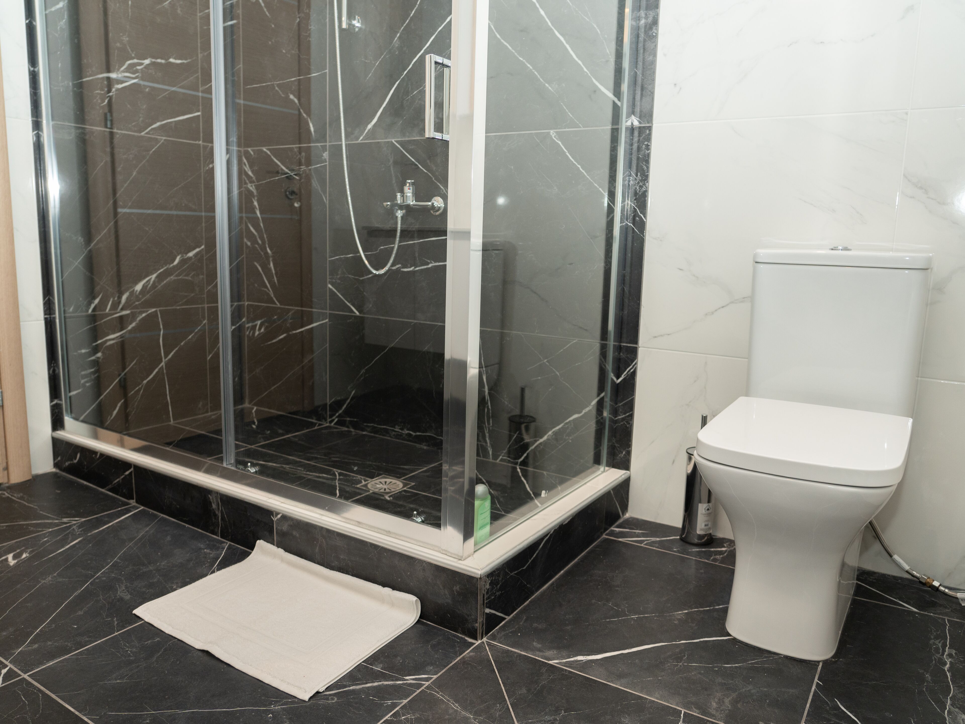 Un baño con ducha de vidrio, inodoro blanco y suelo de mármol negro.
