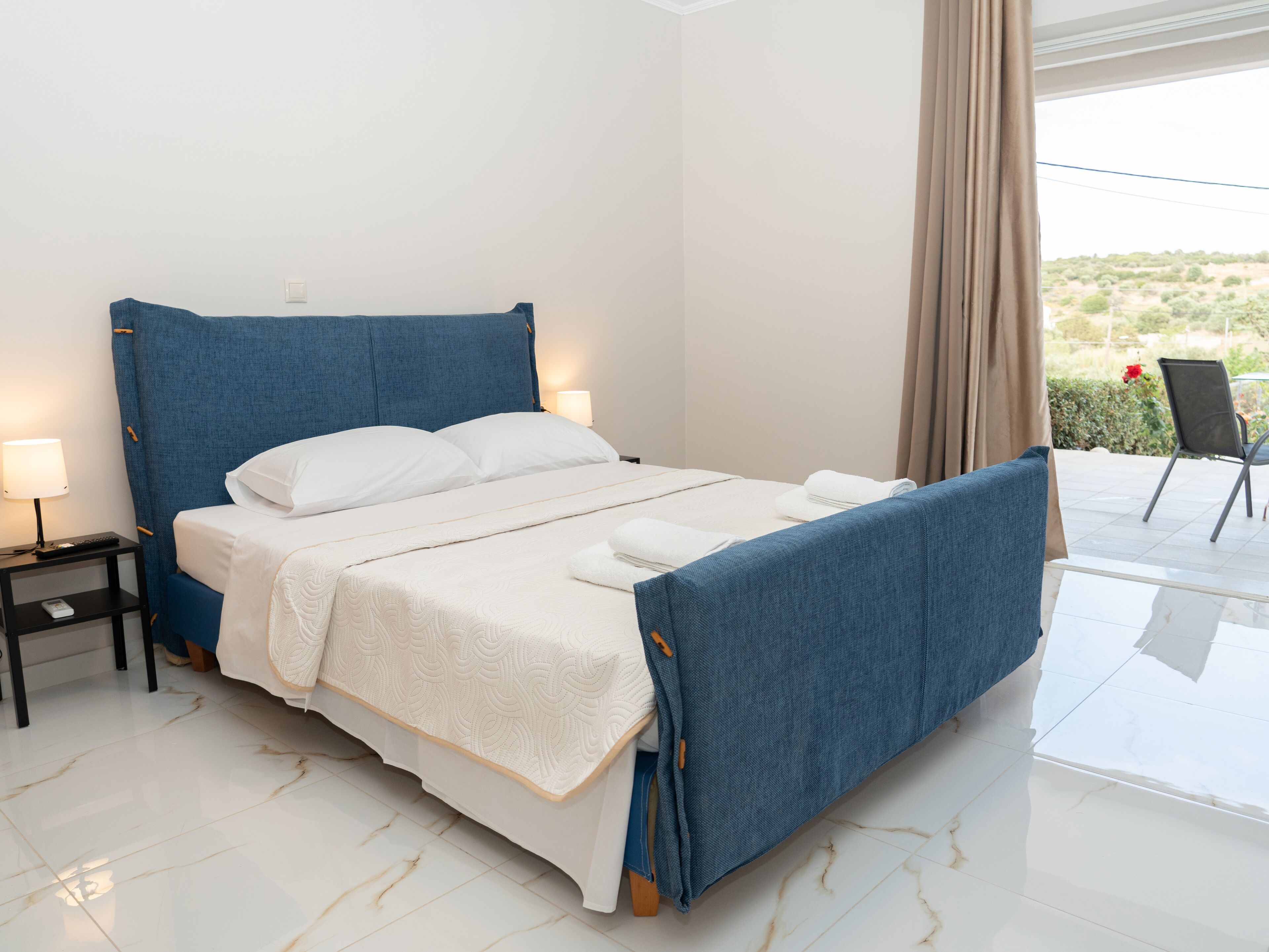 Una cama bien hecha con cabecera azul, ropa de cama blanca y una mesita de noche con lámpara.